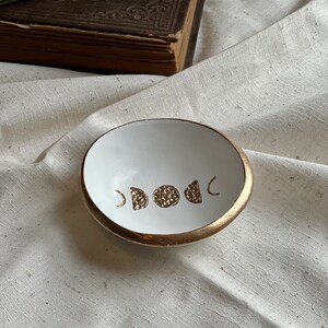 K&ouml;nnte beinhalten: Wei&szlig;e Keramik-Ring Schale mit goldfarbenem Rand und einem goldenen Mondphasen-Design.