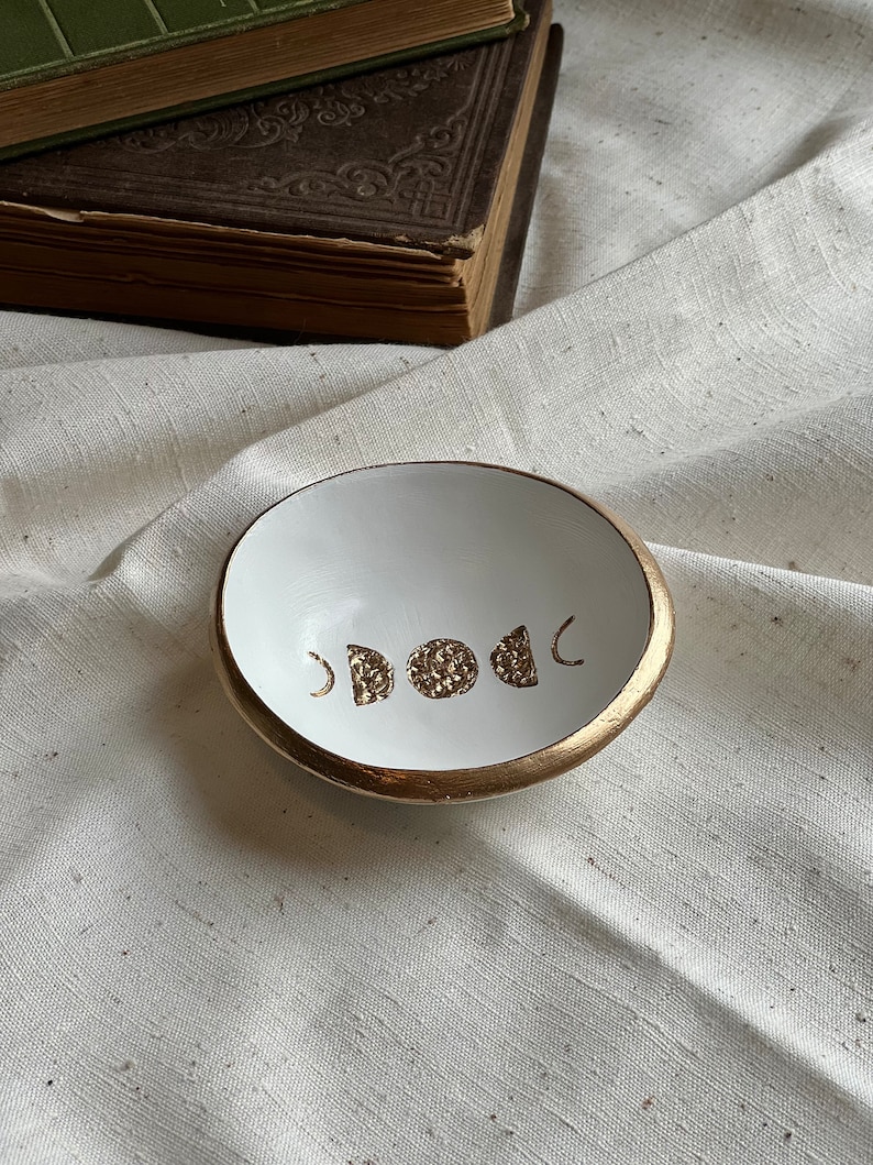 K&ouml;nnte beinhalten: Wei&szlig;e Keramik-Ring Schale mit goldfarbenem Rand und einem goldenen Mondphasen-Design.