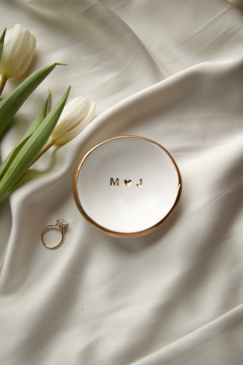 May include: White ceramic ring dish with a gold rim. The dish has the initials "M &hearts; J" written in gold lettering.