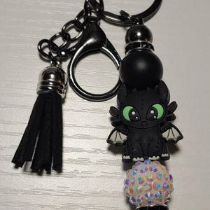 May include: Black and green dragon charm keychain with a black tassel, a white iridescent bead, and a black metal bead.