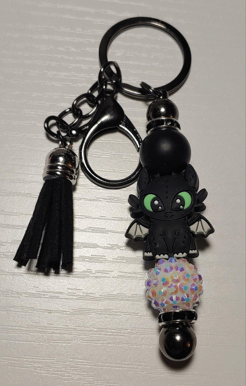 May include: Black and green dragon charm keychain with a black tassel, a white iridescent bead, and a black metal bead.