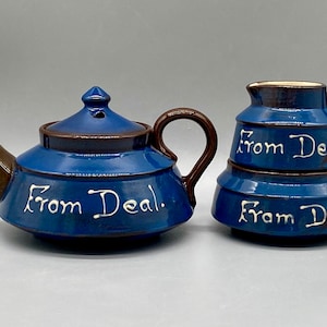 May include: A blue and brown ceramic teapot and creamer set with the words "From Deal." written in white on each piece.