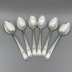 May include: Six silver spoons with ornate handles. The spoons are arranged in a semi-circle with the handles pointing towards the center.