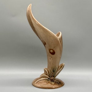 May include: A brown ceramic vase with a unique curved design and a pine cone motif. The vase is glazed in a light brown color with darker brown accents.