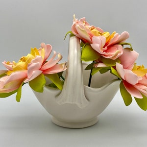 May include: A white ceramic basket with a handle, filled with pink and yellow flowers.