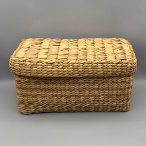 May include: A rectangular storage box with a lid, constructed from woven light brown natural fibers. The box features a consistent, tight braided pattern across the exterior surfaces, including the top of the lid and the four vertical sides.