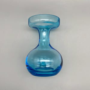 May include: A clear, light blue glass vase with a rounded base and a flared top. The vase has a long, slender neck connecting the base to the top. The glass is smooth and reflects light, creating a vibrant, eye-catching appearance. The vase is a decorative item.