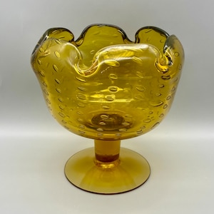 May include: A yellow glass bowl with a textured surface and a scalloped rim. The bowl sits on a pedestal base.