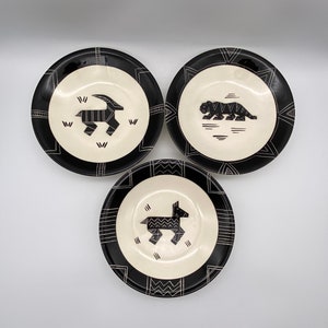 May include: Set of three black and white ceramic plates with geometric designs. Each plate features a different animal silhouette: a goat, a tiger, and a deer.