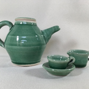 May include: A green ceramic teapot with a matching teacup and creamer. The set is hand-crafted and has a rustic, handmade look.