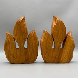May include: Two wooden flame sculptures, each with three points, carved in a light brown color.