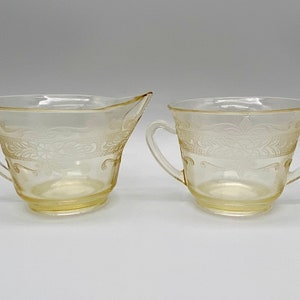 May include: A set of two clear glass sugar and creamer bowls with a delicate floral pattern. The bowls have two handles each and are made of a translucent glass.
