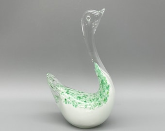 May include: A decorative glass swan figurine. The swan features a white body with green speckled accents and a clear, elongated neck and head. The elegant design is suitable for home decor.