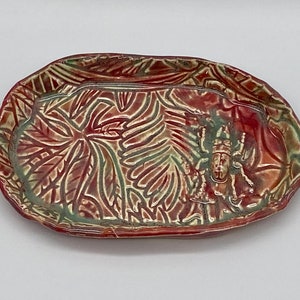 May include: A red and green ceramic dish with a raised design of leaves and a stylized insect in the center.
