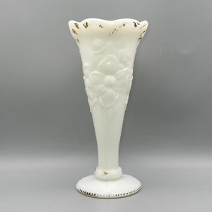 May include: A white milk glass vase with a ruffled top and a floral design. The vase has a gold trim around the top and bottom.