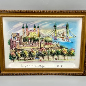 May include: A framed ceramic relief depicting the Tower of London and Tower Bridge. The artwork features a gold-colored frame and a detailed, colorful illustration of the iconic landmarks. The text "Tower of London and Tower Bridge" is visible at the bottom.