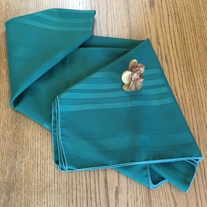 May include: A folded green tablecloth with a striped pattern. The tablecloth is made of a textured fabric and has a subtle sheen.