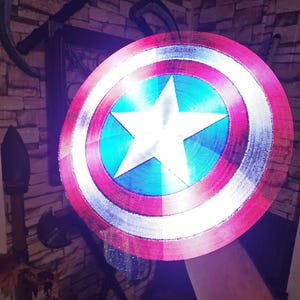 May include: A red, white, and blue Captain America shield with a white star in the center. The shield is made of plastic and has a 3D printed design.