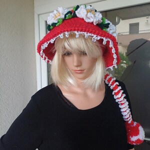 May include: A red crochet hat with white floral detailing and a white beaded trim. The hat features a long, decorative tail in red and white. A unique, handmade accessory.