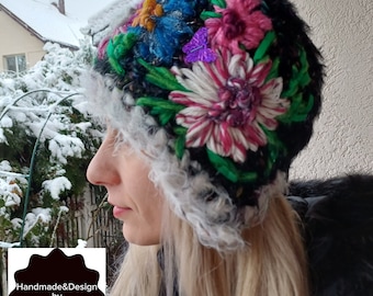 Puede incluir: Un gorro de invierno negro y peludo con un borde de piel sintética blanca. El gorro está decorado con flores bordadas en tonos de rosa, azul, verde y amarillo. El gorro tiene un adorno de mariposa. El texto "Handmade&Design by AnnelieseNicoara" es visible en la imagen.