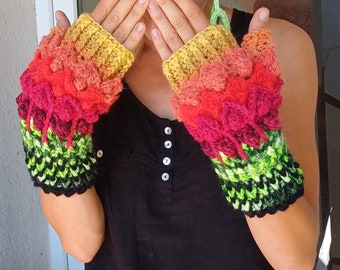 May include: A pair of colourful fingerless gloves with a crocheted design. The gloves are made with a gradient of yellow, orange, red, pink, green and black yarn.