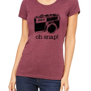 May include: A maroon t-shirt with a black and white image of a vintage camera and the text "oh snap!"