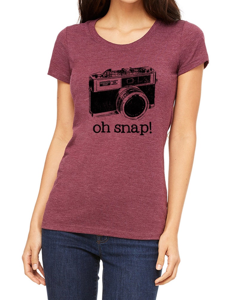 May include: A maroon t-shirt with a black and white image of a vintage camera and the text "oh snap!"