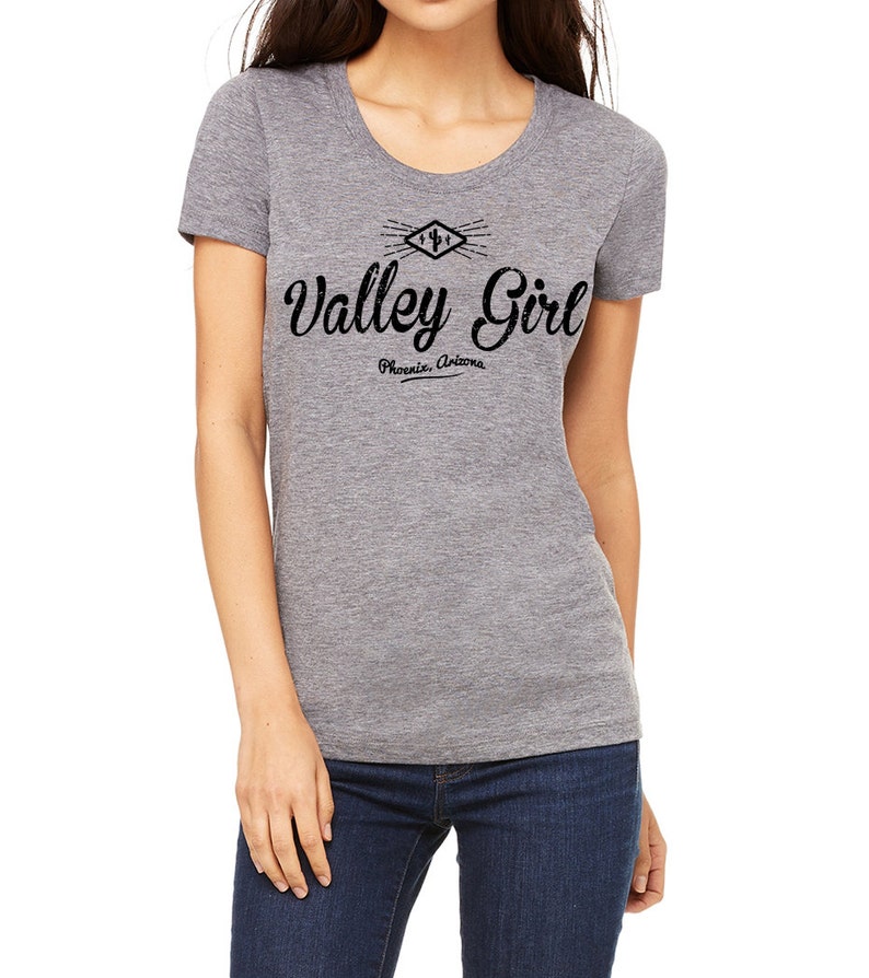 May include: A heather grey t-shirt with a black graphic design featuring a stylized cactus and the text "Valley Girl Phoenix, Arizona".