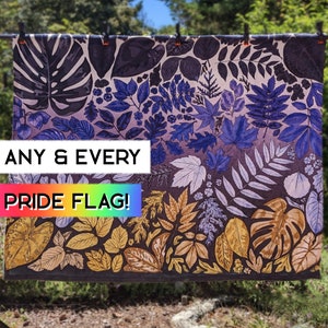Op de afbeelding: Een rechthoekige Pride-vlag met een botanisch ontwerp. De vlag toont bladeren in goud, bruin, blauw en paars. De tekst "ANY & EVERY PRIDE FLAG!" wordt in wit en regenboogkleuren weergegeven.