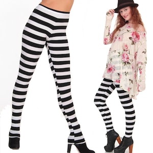 Peut inclure: Leggings rayés noir et blanc à taille haute. Les leggings sont présentés sur deux mannequins, l'un portant un haut fleuri et un chapeau, l'autre portant un haut uni.