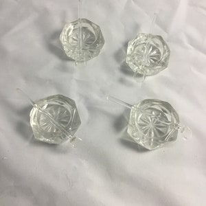 May include: Set of four clear glass salt cellars with matching clear glass spoons. Each cellar has a faceted design and a round base.