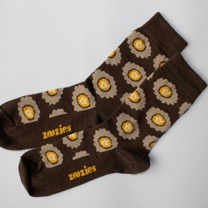 以下が含まれることがあります： ベージュと黄色の花柄の茶色の靴下2足組。靴下には黄色で「Zozies」と書かれています。