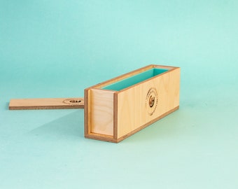 May include: A wooden soap mold with a removable lid. The mold is made of light wood and has a blue silicone liner. The mold is labeled "Handmade with Love" and has a logo of a stylized "GH".