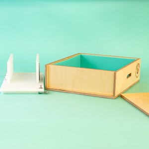 May include: A white plastic soap cutter with a clear plastic cutting guide and a wooden box with a teal blue liner. The box is open and the lid is off to the side.