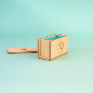 May include: A wooden soap mould with a light blue silicone liner. The mould is open and the lid is lying next to it. The mould has the text "Workshop Series" and "Made in USA" printed on the side.