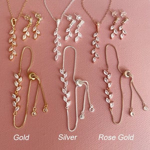 K&ouml;nnte beinhalten: Drei Schmucksets in Gold-, Silber- und Ros&eacute;goldt&ouml;nen, bestehend aus einer Halskette, einem Paar Ohrh&auml;ngern und einem verstellbaren Armband. Jedes St&uuml;ck ist mit klaren, marquisef&ouml;rmigen Steinen in einem blattartigen Muster verziert.
