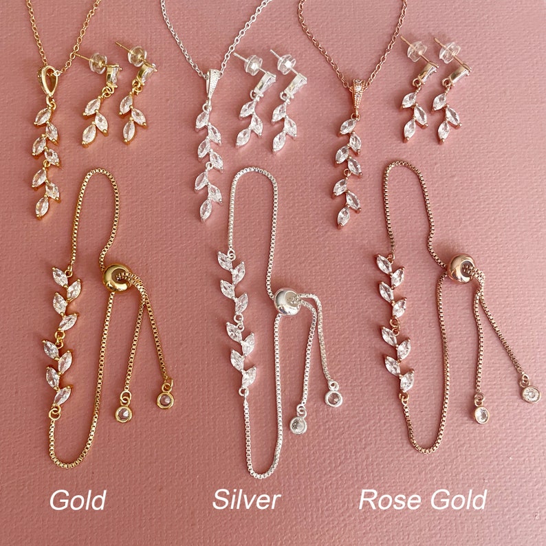 K&ouml;nnte beinhalten: Drei Schmucksets in Gold-, Silber- und Ros&eacute;goldt&ouml;nen, bestehend aus einer Halskette, einem Paar Ohrh&auml;ngern und einem verstellbaren Armband. Jedes St&uuml;ck ist mit klaren, marquisef&ouml;rmigen Steinen in einem blattartigen Muster verziert.