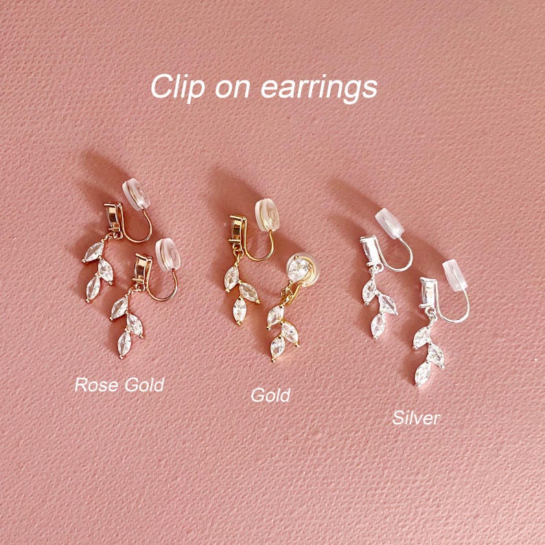 May include: Three pairs of clip-on earrings in rose gold, gold, and silver tones. Each earring features a dangling leaf-shaped design adorned with clear marquise-cut stones and a clear silicone cushion pad on the clip mechanism. Text reads Clip on earrings, Rose Gold, Gold, and Silver.