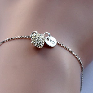 Può includere: Un braccialetto a catena d'argento con un piccolo ciondolo rotondo e testurizzato e un ciondolo rotondo con il numero "72" inciso su di esso.