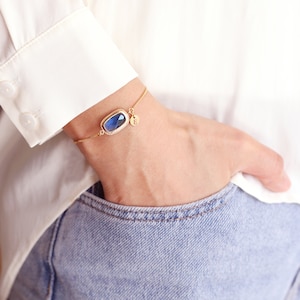 May include: A gold chain bracelet with a blue gemstone and a small charm with the letter "E" on it.