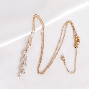 May include: A gold-toned necklace featuring a delicate chain and a vertical pendant composed of five marquise-cut clear stones arranged in a leaf-like pattern. The chain includes a small circular clasp and an adjustable length mechanism.