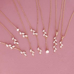 Könnte beinhalten: Eine Sammlung von sechs goldfarbenen Halsketten mit zarten Ketten und blattförmigen, klaren Kristallakzenten. Einige Designs enthalten kleine weiße Perlen oder im Markisenschliff geschliffene Steine, die in rankenartigen Mustern angeordnet sind.