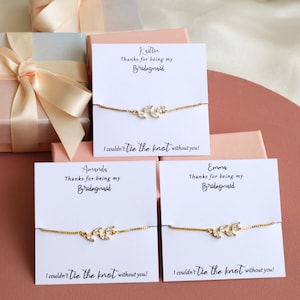 May include: Three gold-tone chain bracelets with leaf-shaped clear crystal accents, each mounted on a white card printed with the names Kaitlin, Amanda, or Emma, the text Thanks for being my Bridesmaid, and I couldn't tie the knot without you!