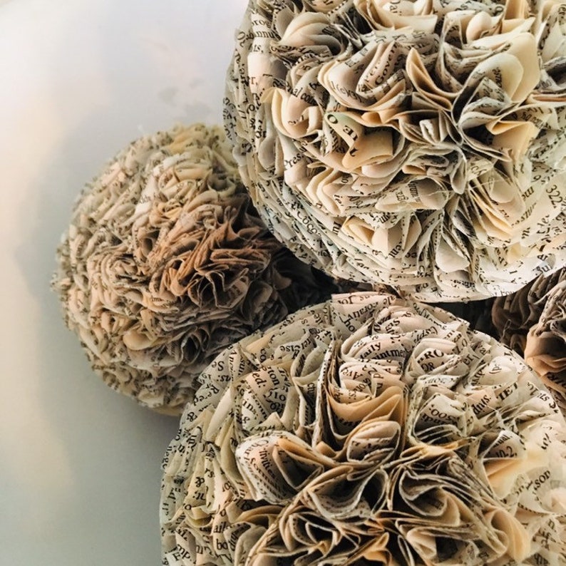 K&ouml;nnte beinhalten: Drei cremefarbene Papierkugeln aus Seiten eines alten Buches. Das Papier ist gekr&auml;uselt und gefaltet, um eine blumenartige Form zu erzeugen.