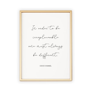 May include: A gold framed print with a white background and black text that reads "In order to be irreplaceable one must always be different." The text is in a cursive font. The bottom of the print reads "COCO CHANEL".