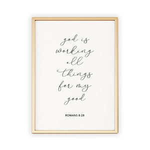 May include: A gold framed print with a white background and black calligraphy text that reads "god is working all things for my good" with the scripture reference "Romans 8:28" below.