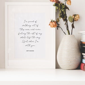 May include: A framed print with a white background and black text. The text reads: "I'm scared of walking out of this room and facing the rest of my whole life the way I feel when I'm with you." The text is signed "Dirty Dancing". The print is on a white shelf with a vase of dried flowers and a stack of books.