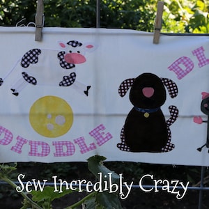 May include: A white fabric banner with the words "Hey Diddle Diddle" in pink letters with a checkered pattern. The banner features a yellow cat holding a violin, a black and white cow, a black dog, a stick figure with a spoon, and a blue and white plate with a face.