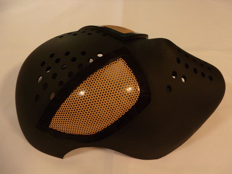 Puede incluir: M&aacute;scara de Halloween negra y naranja con un dise&ntilde;o de ojo de malla. La m&aacute;scara tiene una superficie texturizada y est&aacute; hecha de pl&aacute;stico duro.