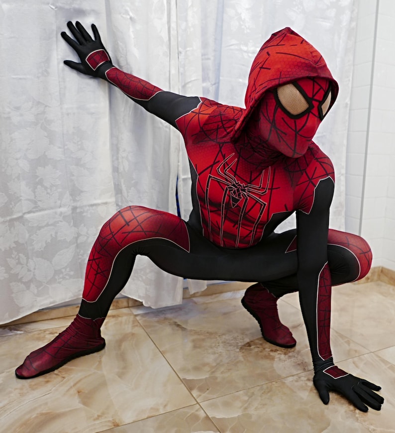 Puede incluir: Un traje de superh&eacute;roe de spandex rojo y negro con un dise&ntilde;o de telara&ntilde;a. El traje incluye una m&aacute;scara con capucha con un dise&ntilde;o de telara&ntilde;a y un logotipo de ara&ntilde;a rojo y negro en el pecho.